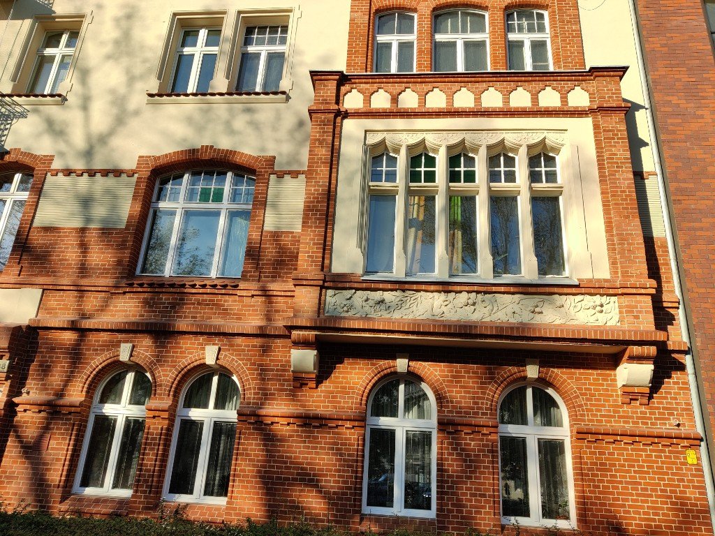 Zdobione okna łukowe z kamiennymi detalami i fryzem roślinnym na elewacji ceglanej